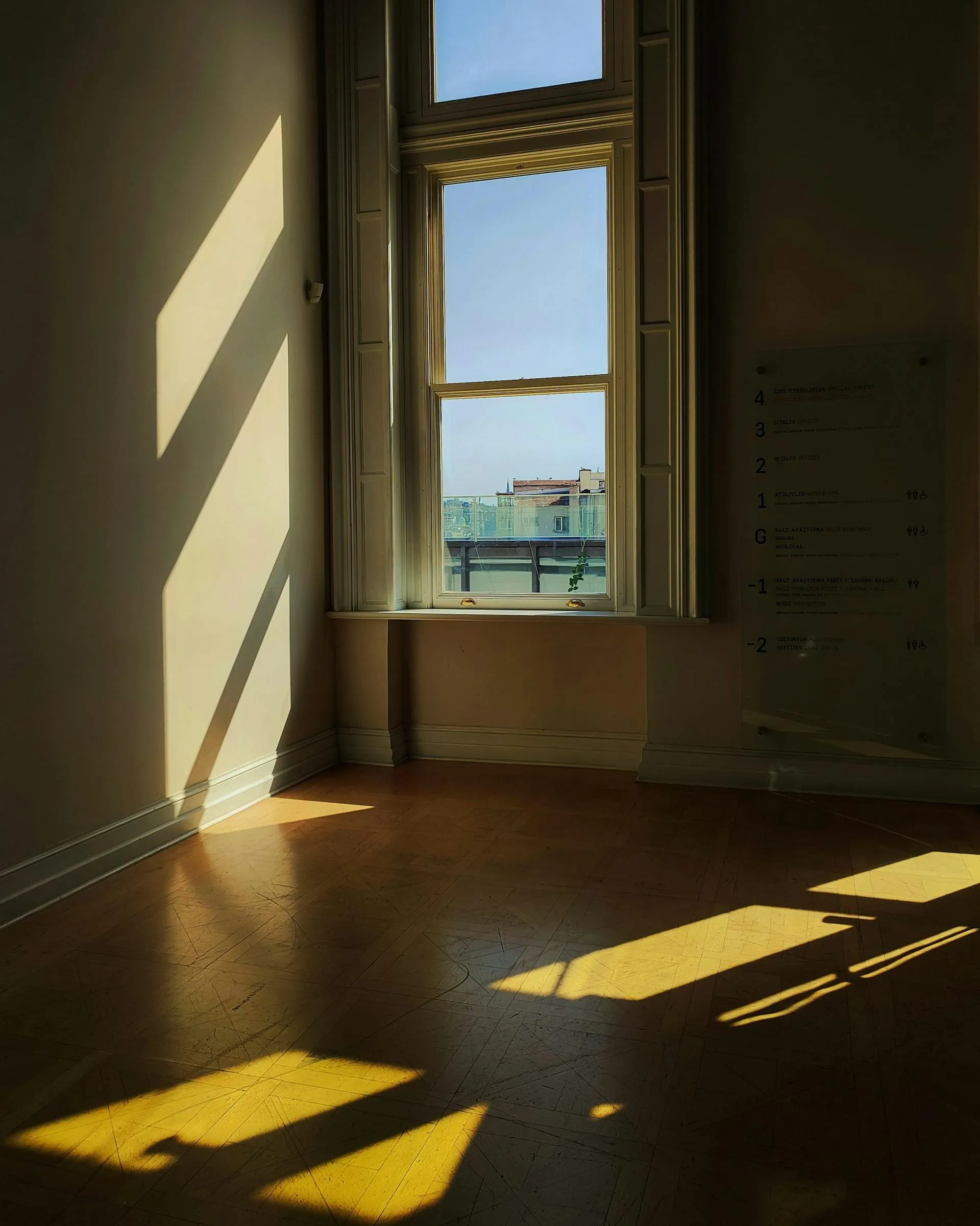 Empty interior with intense afternoon sunlight pouring through a tall window casting long sharp shadows on the floor