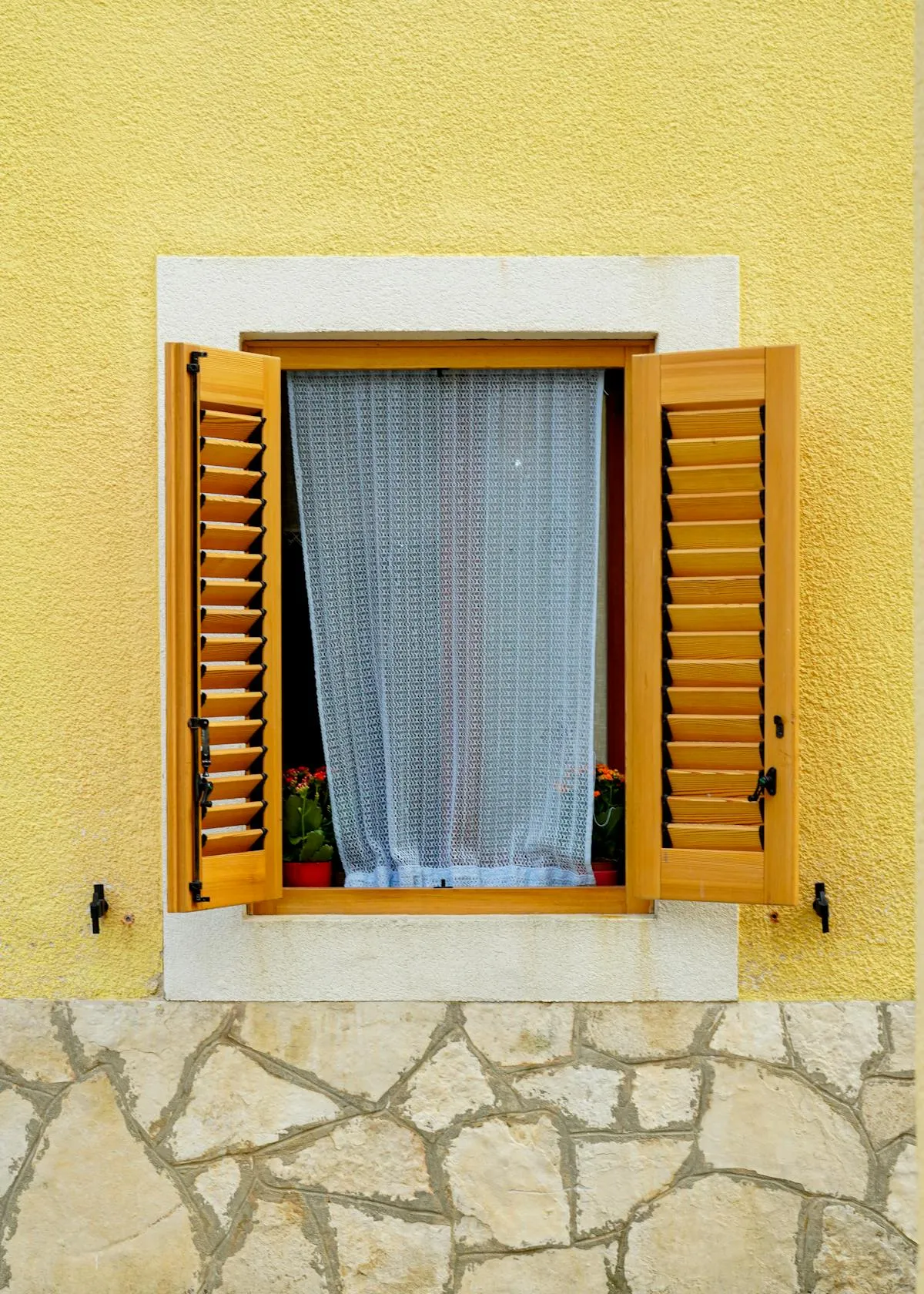 Sheer curtain in window with open wooden window shutters showing the traditional alternative to interior film treatments