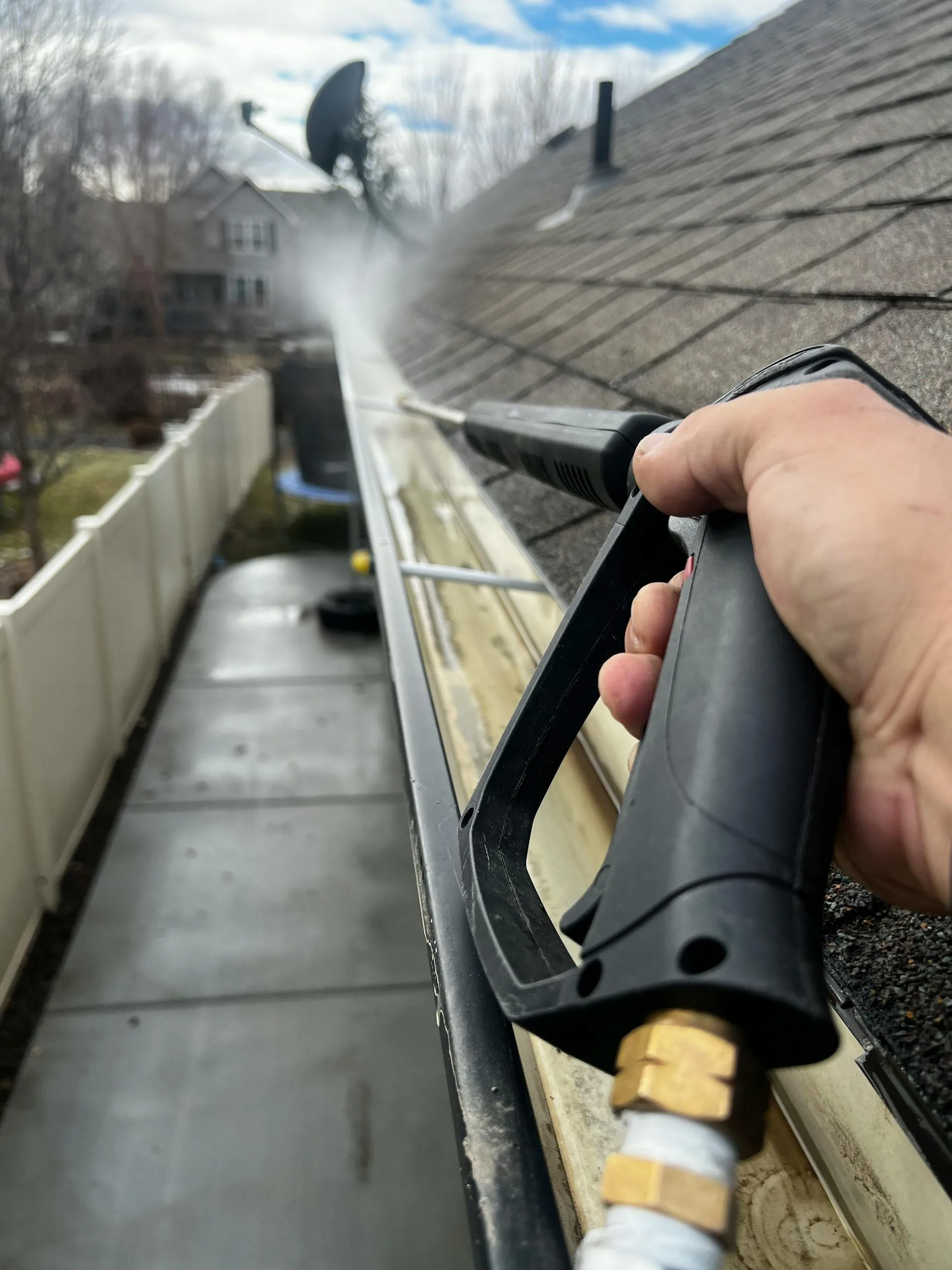 Close-up of residential gutter being cleaned with a pressure washer attachment in bright outdoor light