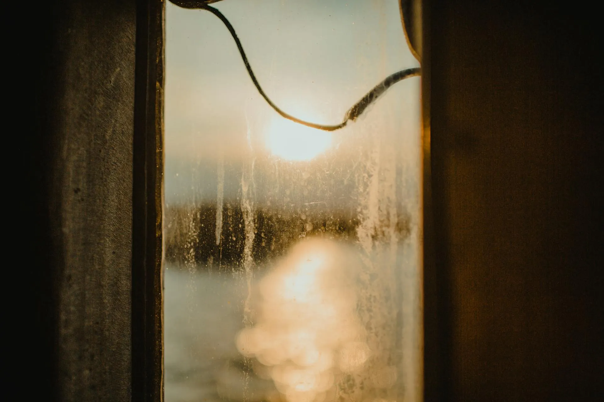Window pane covered in mineral spotting and water stains catching strong sunset light — the textbook look of hard-water etch