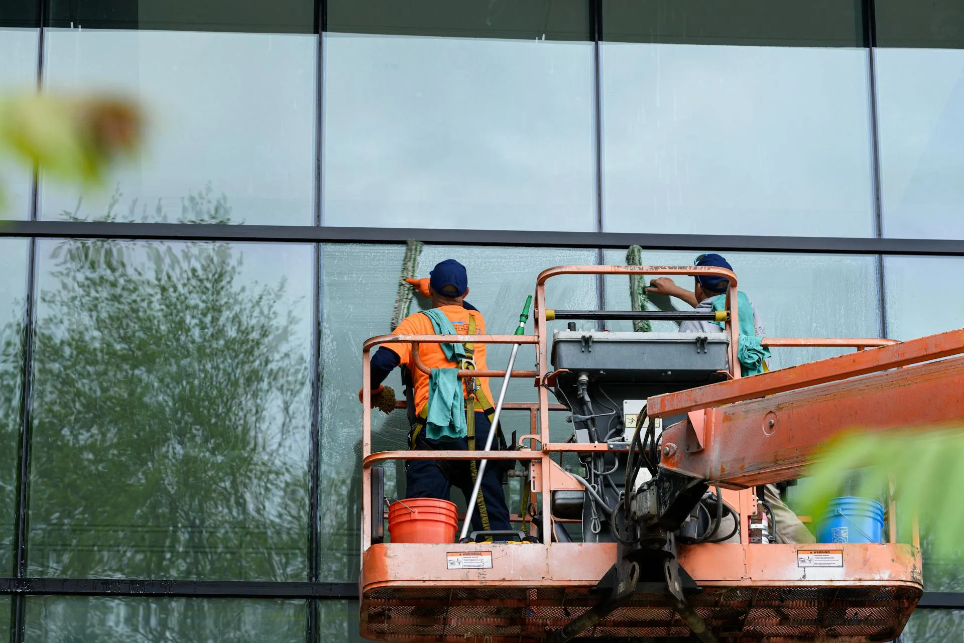 Two professional window cleaners on an elevated work platform cleaning the glass facade of a modern commercial building