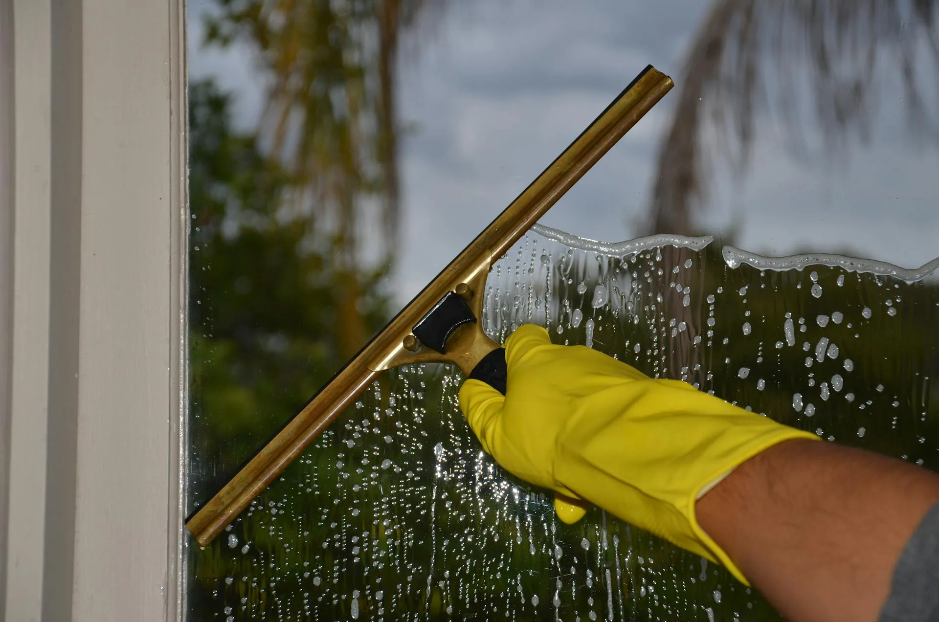 Close-up of a hand in yellow rubber glove using a professional squeegee to clean glass with even pressure
