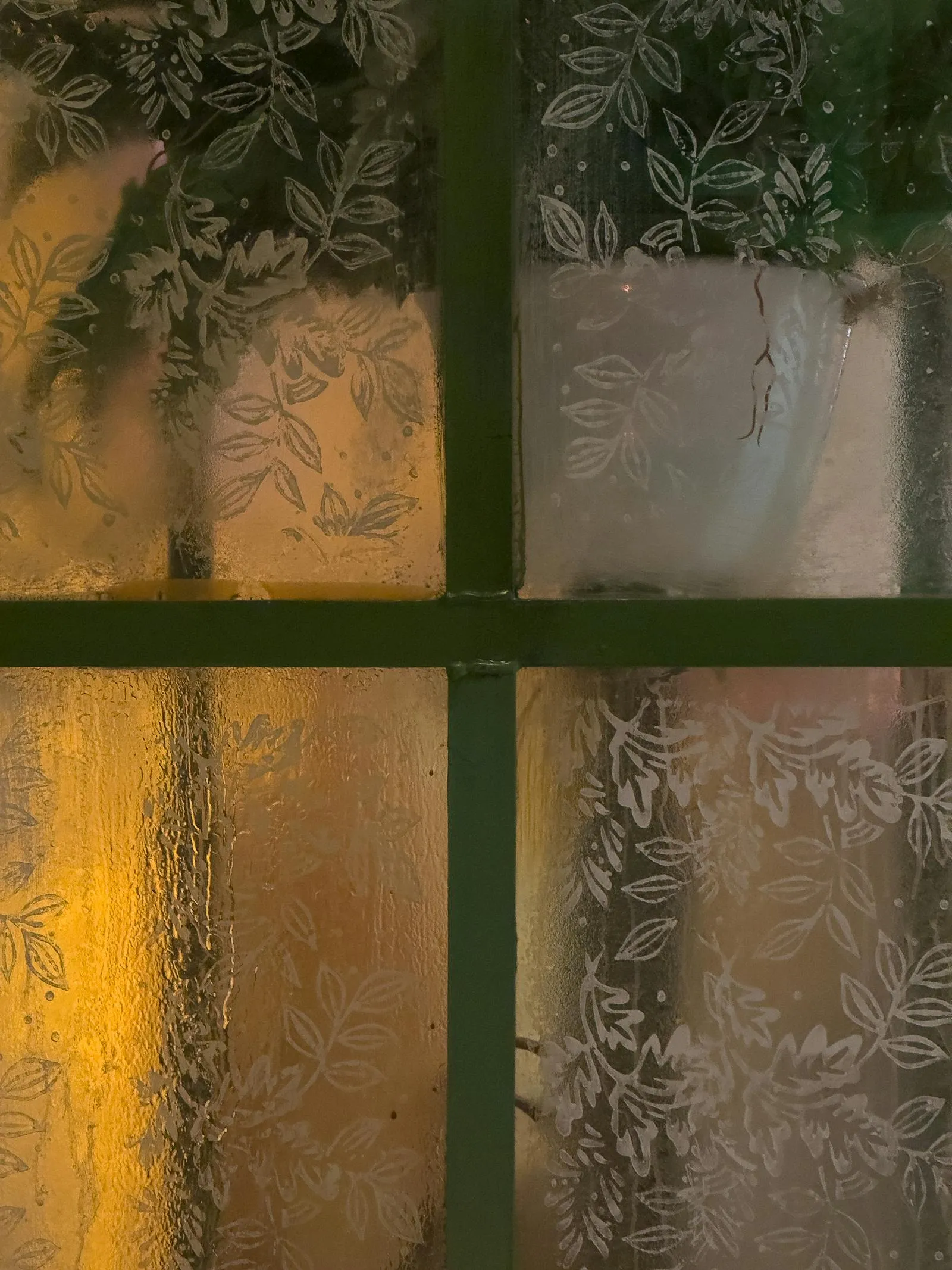 Frosted privacy film with delicate leaf pattern on a window with warm light glowing through the textured glass